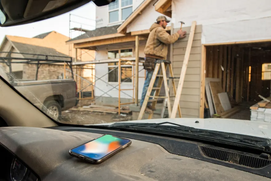 A phone lighting up on a truck dashboard while a builder works on a ladder outside